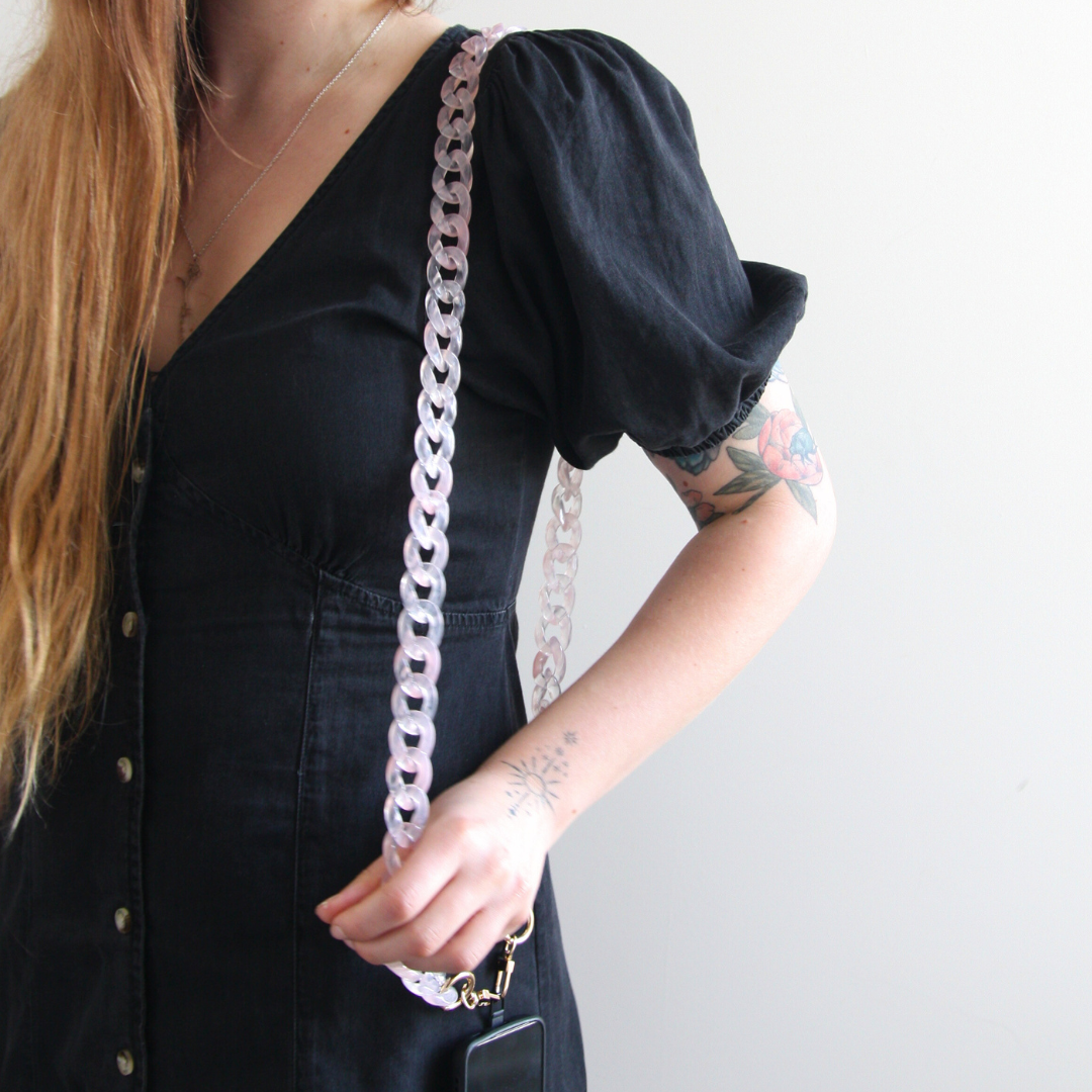 Girl with blond hair standing and showing her pink transparant crossbody phone strap.